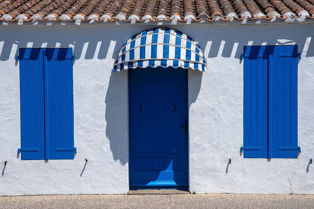 Facciata bianca con persiane blu e tenda a righe